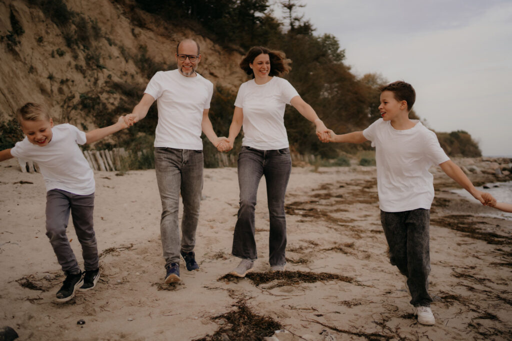 Familie läuft lachend am Strand entlang und hält sich an den Händen